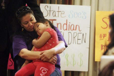 Madonna Pappan, top, hugs her 4-year-old daughter Charlie Pappan before speaking at a press conference at the Adobe Eco Hotel in Rapid City, S.D. on Thursday, March 21, 2013. Pappan is one of three mothers represented by the American Civil Liberties Union in a class action suit filled by the ACLU on behalf of the Rosebud Sioux and Oglala Sioux tribes. The tribes are challenging the state's practices and policies that they say violate the Indian Child Welfare Act.  (AP Photo/Rapid City Journal, Kristina Barker)