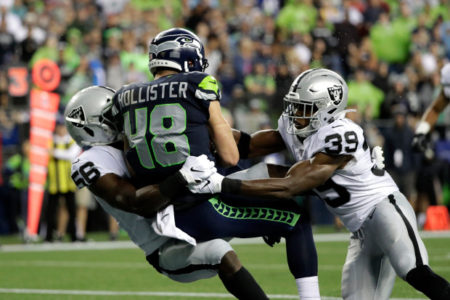 Seattle Seahawks tight end Jacob Hollister (48) scores a touchdown after a reception as he is tackled by Oakland Raiders' Te'Von Coney, left, and Jordan Richards, right, during the first half of an NFL football preseason game Thursday, Aug. 29, 2019, in Seattle. (AP Photo/Elaine Thompson)