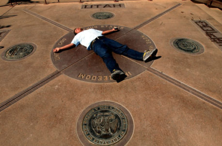 Four Corner Monument,AZ, Navajo Nation: slug:Fourcorners- Spread over four States, Heath Jackson  of Colorado Springs, CO goofs for the camera of his traveling companions, as they make a brief visit to the Four Corners Monument marking the only spot where four States meet.The survey that marked the boundaries of SE Utah, NE Arizona, SW Colorado and NW New Mexico was undertaken in 1868 and completed correctly in 1875, the dedication of a Four Corners National Monument occurred in September 1962. This is the 40th year for the monument

Staff Photo Shaun Stanley