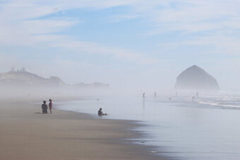 FILE - People walk on the beach at Tierra del Mar, Ore., on, Aug. 17, 2020. The Oregon Coast is featured in a collection of mini-essays by American writers published online by the Frommer's guidebook company about places they believe helped shape and define America.  (AP Photo/Andrew Selsky, File)