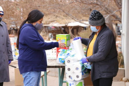 Miyoshi Lee, left, and Leslie Goldtooth, right, aid residents with some basic relief goods at the Full Circle Intertribal Center in Moab, Utah on Dec. 17, 2020. They said joining the group has helped them find a sense of community, where they've both lived for over two decades. The Utah-based nonprofit was founded to help build community among the Native population in Moab and has recently turned its attention to caring for Native elders during the coronavirus pandemic. (Kate Groetzinger/KUER, via AP)