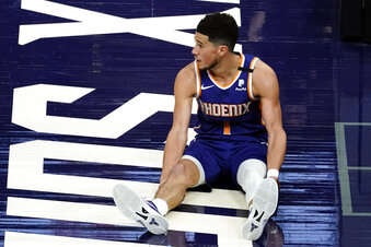 Phoenix Suns guard Devin Booker watches as play continues after he was knocked to the floor during the second half of the team's NBA basketball game against the Golden State Warriors on Thursday, March 4, 2021, in Phoenix. (AP Photo/Rick Scuteri)