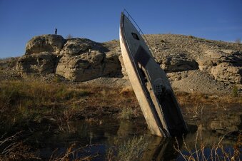 A man stands on a hill overlooking a formerly sunken boat standing upright into the air with its stern buried in the mud along the shoreline of Lake Mead at the Lake Mead National Recreation Area, Friday, Jan. 27, 2023, near Boulder City, Nev. Competing priorities, outsized demands and the federal government's retreat from a threatened deadline all combined to thwart a voluntary deal last summer on how to drastically cut water use from the parched Colorado River, according to emails obtained by The Associated Press. (AP Photo/John Locher)