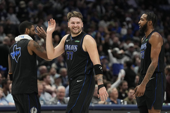 Dallas Mavericks guard Luka Doncic (77) smiles as he comes off the floor past teammate Kyrie Irving, left, and forward Derrick Jones Jr. (55) during the first half of an NBA basketball game against the Utah Jazz in Dallas, Wednesday, Dec. 6, 2023. (AP Photo/LM Otero)